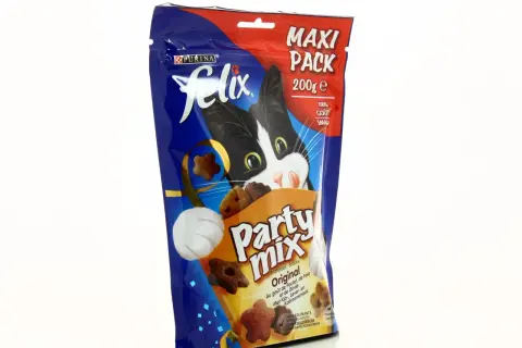 Un chat noir et blanc curieux regarde un paquet de friandises Felix Party Mix, parfait pour l'alimentation mixte chat.