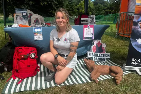 Une femme présente un stand sur la fibrillation canine, avec un mannequin de chien et du matériel de premiers secours. Elle enseigne le massage cardiaque chien.