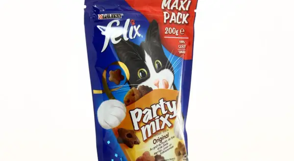Un chat noir et blanc curieux regarde un paquet de friandises Felix Party Mix, parfait pour l'alimentation mixte chat.