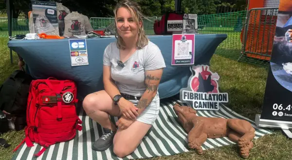 Une femme présente un stand sur la fibrillation canine, avec un mannequin de chien et du matériel de premiers secours. Elle enseigne le massage cardiaque chien.