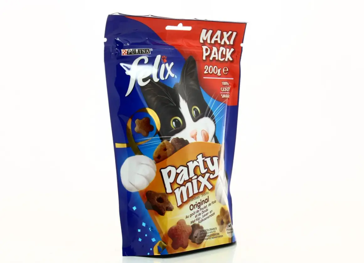 Un chat noir et blanc curieux regarde un paquet de friandises Felix Party Mix, parfait pour l'alimentation mixte chat.