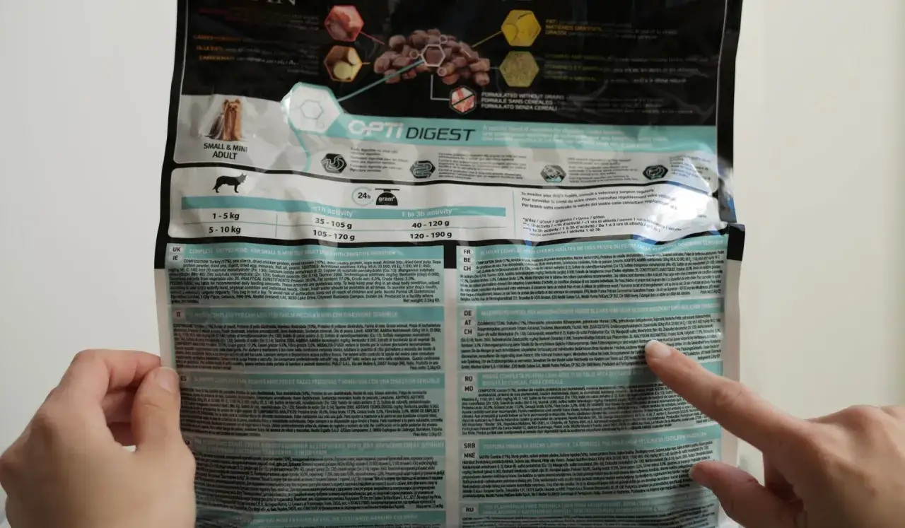 Un sac de croquettes pour chien, avec une main qui pointe vers la liste des ingrédients. La mention